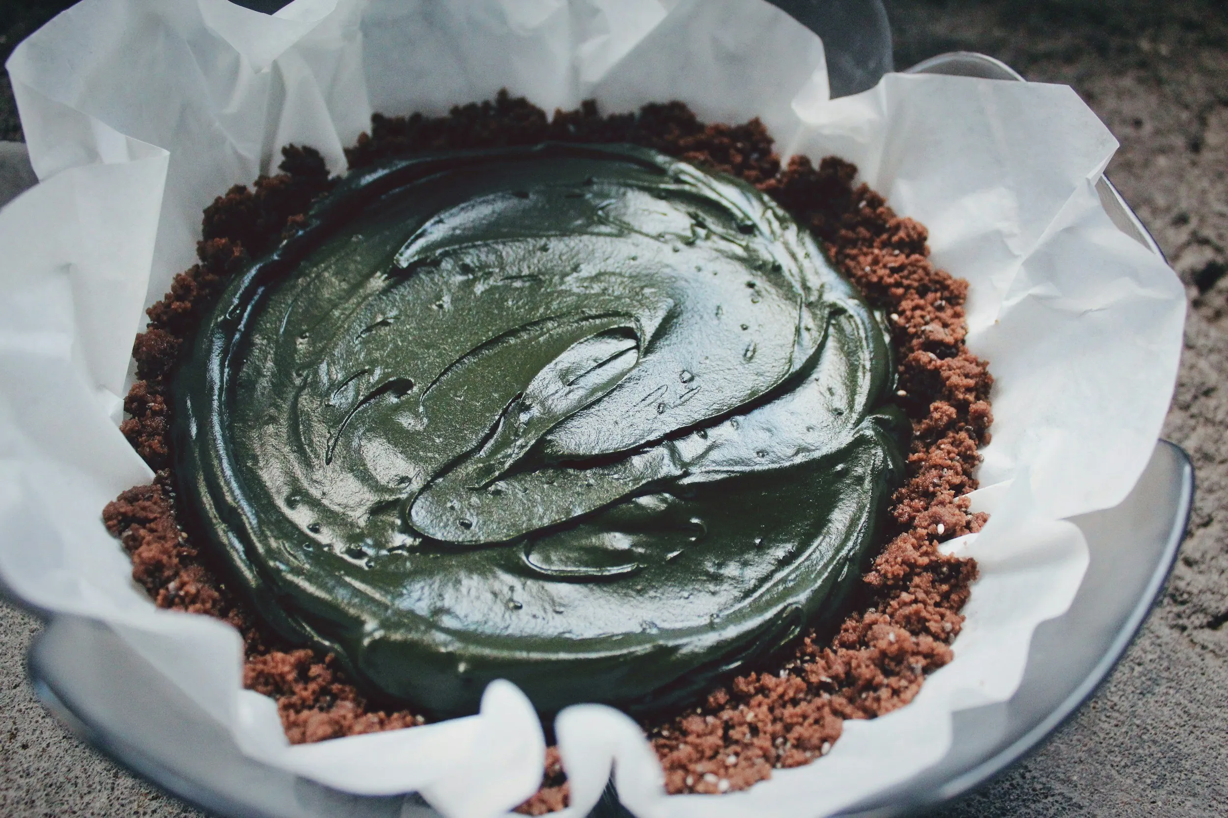 A parchment-lined bowl of deep green spirulina paste resting on dark soil.