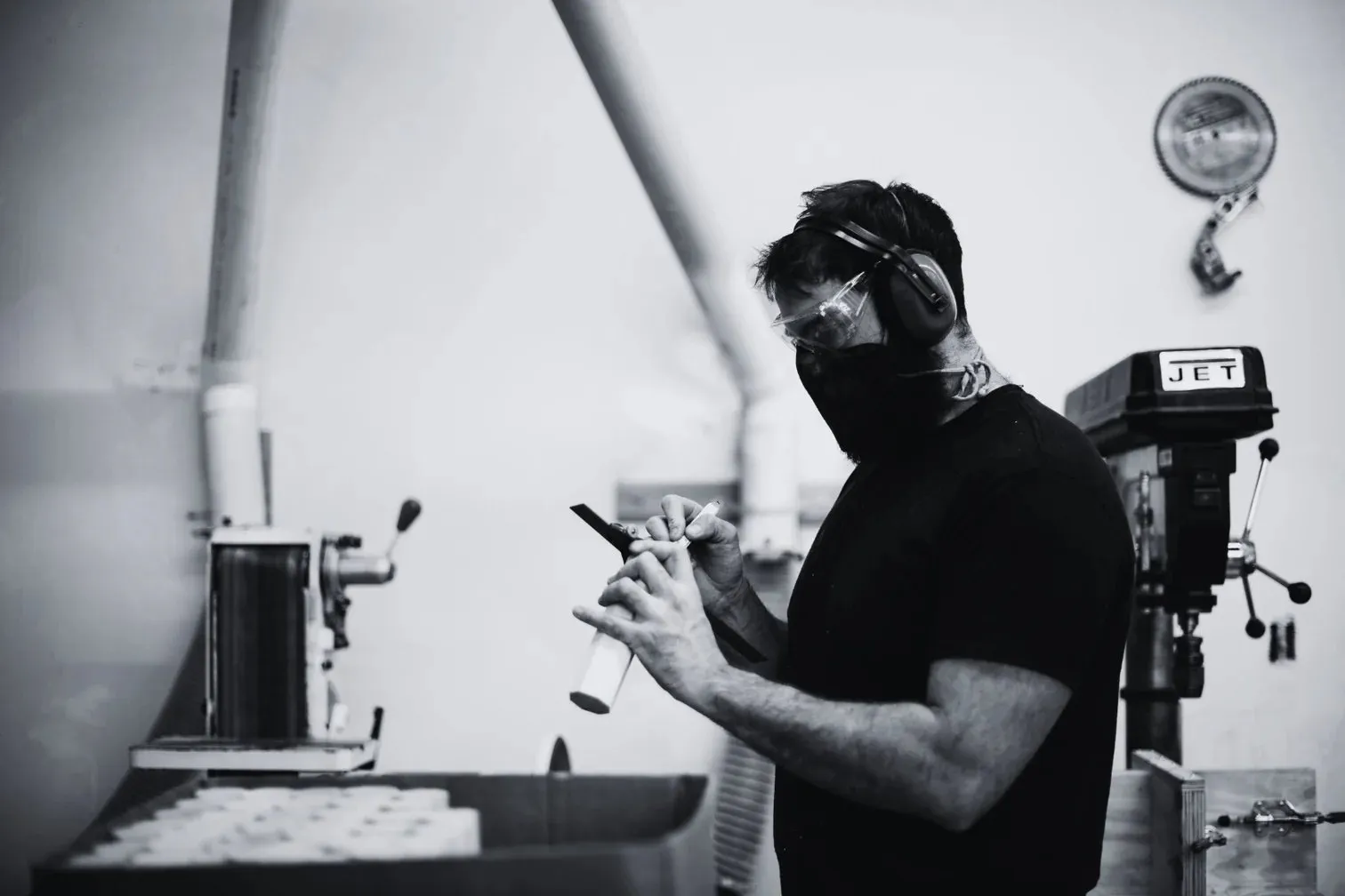 A maker in a workshop operating a drill press, in black and white.